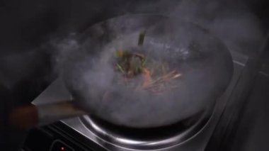 Sıcak tavada pişen sebzeli ramen. Şef, bu profesyonel mutfak ortamında Asya mutfağının özünü yakalama konusunda ustaca karıştırıyor..