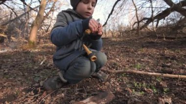 Genç bir çocuk ormanda çalı ustalığı becerileri geliştiriyor. Bıçakla sopayı dikkatlice oyuyor. Bu video açık havada öğrenme ve hayatta kalma becerilerini doğal ortamlarda yakalar..