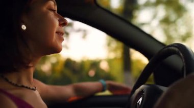 Bir kadın gün batımında kırsalda rahat bir şekilde araba sürmekten zevk alır. Kolunu camdan dışarı uzatıp, huzurlu bir özgürlük ve huzur anı yakalar..