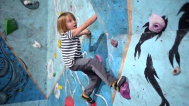 6 yaşında bir çocuk canlı, kapalı bir tırmanma duvarında kayaya çarpmış. Odaklanmış ve çevik. Renkli tutuş, denge ve tekniği ustalıkla gösteriyor..