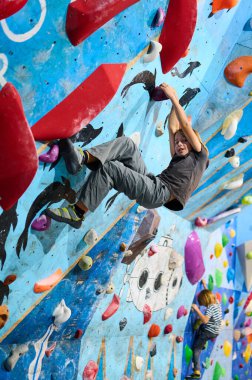 A 10-year-old boy climbing on a colorful indoor bouldering wall, focused on reaching the next hold. Active lifestyle and sport for kids clipart