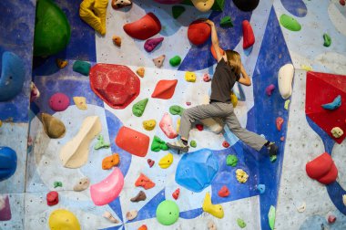 A 10-year-old boy climbing on a colorful indoor bouldering wall, focused on reaching the next hold. Active lifestyle and sport for kids clipart