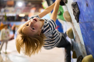 6 yaşında bir çocuk tırmanmaya odaklanmış, dikkatli bir şekilde kapalı bir kaya duvarına tutunuyor. Renkli ambarlar ve detaylı konsantrasyon kararlılığını gösteriyor..