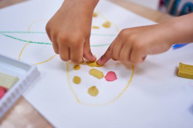 Childs 'ın elleri kağıt üzerinde kil parçalarıyla çalışıyor, bir sanat projesi yaratıyor. Renkli kil ve çizgiler görünür, yaratıcılığı ve ince motor becerileri teşvik eder.