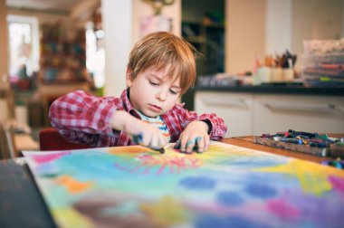 Young boy in a plaid shirt drawing with colorful pastels on a large sheet of paper at home. Focused on creative activity in a cozy art space. clipart