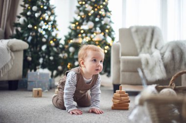 Güzel dekore edilmiş Noel ağaçları ve hediye paketleriyle çevrili, yumuşak halıda sürünen bir bebek, sıcak bir tatil ortamı yaratıyor..