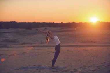 Gün batımında çöl manzarasında yoga yapan bir insan güneş batarken doğayla olan huzurunu ve bağlantısını kucaklıyor..