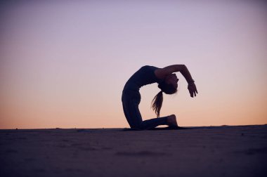 Bir kadın gün batımında yoga pozu veriyor ve gökyüzüne çarpıcı bir siluet yaratıyor. Huzurlu ortam, doğada huzur ve odaklanma duygusunu arttırır..