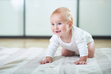 Mavi gözlü neşeli bir bebek, ferah ve aydınlık bir odada açık renkli bir paspasın üzerinde emekliyor. Bebek meşgul görünüyor ve etrafındakileri merak ediyor..