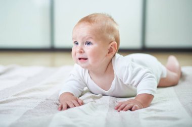 Bir bebek, aydınlık bir odada dokulu bir battaniyenin üzerinde emekleyerek keşfediyor. Çocuğun parlak mavi gözleri ve çevreleriyle etkileşime girerken tuhaf bir ifadesi var..