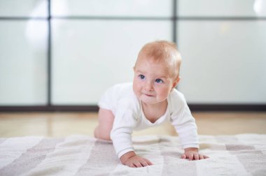 Neşeli bir bebek, kapalı bir alanda çizgili bir halının üzerinde emekler, çevreyi keşfederken merak ve neşe gösterir. Doğal ışık, sahneyi çok güzel aydınlatıyor..