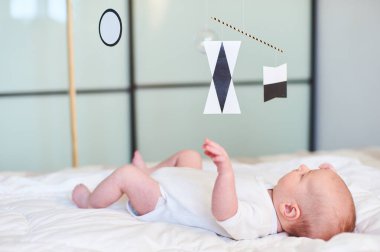 Yeni doğan bebek yumuşak bir yatakta uzanıyor, siyah beyaz bir Montessori Munari aracına uzanıyor, erken görme gelişimini ve bebeklerde duyusal bağlılığı teşvik ediyor..