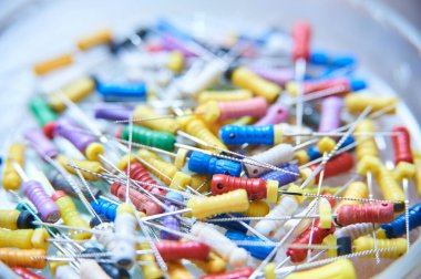 Kanal tedavisi için kullanılan dişçi endodontik dosyalarının renkli bir çeşidi. Bulanık bir arkaplanda çeşitli boyut ve renklere sahip tıbbi araçların yakın çekimleri.