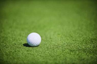 Doğal güneş ışığı altında yemyeşil çimlerde beyaz golf topu, yakın plan, temiz arka plan, mükemmel doku, spor ve eğlence kavramları için uygun..