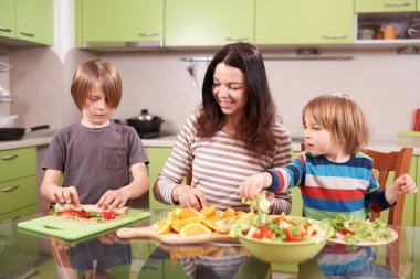 Mutlu aile mutfakta sağlıklı yiyecekler hazırlıyor, anne ve çocuklar paket yapıyor ve sebze kesiyor, takım çalışması, sağlıklı beslenme, parlak ev atmosferi..