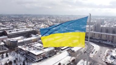 Kharkiv 'in karlı şehir manzarasında gururla dalgalanan Ukrayna bayrağı, insansız hava araçlarının hava perspektifinden çekilmiş, parlak bir kış gününde tarihi mimari ve modern gökyüzünün bir karışımını sergiliyor..