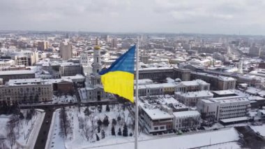 Kharkiv 'in karlı şehir manzarasında gururla dalgalanan Ukrayna bayrağı, insansız hava araçlarının hava perspektifinden çekilmiş, parlak bir kış gününde tarihi mimari ve modern gökyüzünün bir karışımını sergiliyor..