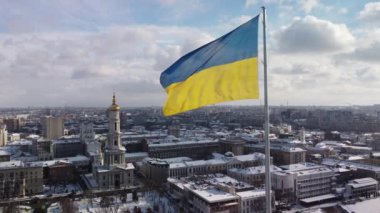 Kharkiv 'in karlı şehir manzarasında gururla dalgalanan Ukrayna bayrağı, insansız hava araçlarının hava perspektifinden çekilmiş, parlak bir kış gününde tarihi mimari ve modern gökyüzünün bir karışımını sergiliyor..