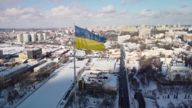 Kharkiv 'in karlı şehir manzarasında gururla dalgalanan Ukrayna bayrağı, insansız hava araçlarının hava perspektifinden çekilmiş, parlak bir kış gününde tarihi mimari ve modern gökyüzünün bir karışımını sergiliyor..