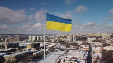 Kharkiv 'in karlı şehir manzarasında gururla dalgalanan Ukrayna bayrağı, insansız hava araçlarının hava perspektifinden çekilmiş, parlak bir kış gününde tarihi mimari ve modern gökyüzünün bir karışımını sergiliyor..