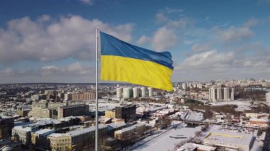 Kharkiv 'in karlı şehir manzarasında gururla dalgalanan Ukrayna bayrağı, insansız hava araçlarının hava perspektifinden çekilmiş, parlak bir kış gününde tarihi mimari ve modern gökyüzünün bir karışımını sergiliyor..