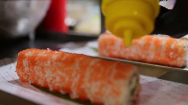 Turuncu tobiko kaplı suşi rulosu, sarı bir şişeden bir parça sos ile süsleniyor. Profesyonel bir mutfakta yemek hazırlamak için yakın plan..