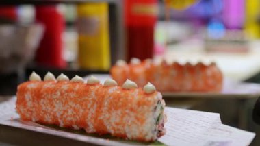 Sos ve kremayla süslenmiş turuncu tobiko kaplı suşi ruloları, sarı bir şişeden serpiştirilen sos, yiyecek sunum sürecine yakın çekim..