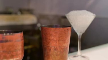 Barmen, arka planda ezilmiş buzla dolu bir martini bardağıyla bakır bir kokteyl bardağına meyve suyu dolduruyor..
