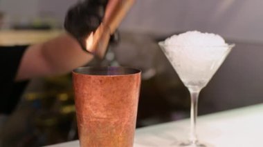 Barmen, arka planda ezilmiş buzla dolu bir martini bardağıyla bakır bir kokteyl bardağına meyve suyu dolduruyor..