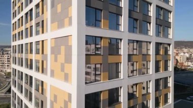 Yüksek katlı bir bina düz çizgiler ve dış görünüşünde benzersiz bir desen sergiliyor. Yapı, şehir yaşamı ve altyapısıyla çevrili temiz bir gökyüzüne karşı dimdik ayakta duruyor..