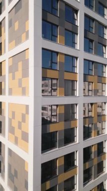 Yüksek bir konut binasında geniş pencereli ve cephesinde canlı geometrik desenleri olan çağdaş bir tasarım sergileniyor. Güneş ışığı camdan yansıyarak yapıların cazibesini arttırır..