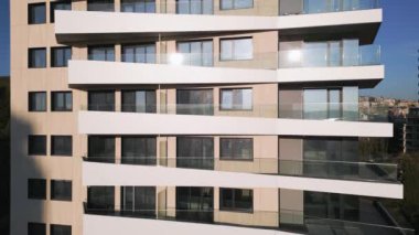 Çağdaş bir apartman dairesi kıvrımlı balkonları ve parlak yüzüyle göze çarpıyor. Güneş ışığı pencerelerden yansıyarak canlı bir kentsel atmosfer yaratır..