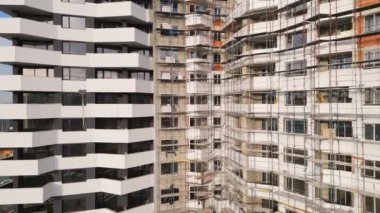 İşçiler aktif olarak çağdaş bir konut inşaatı ile meşguller. İskeleler birden fazla katı çevreleyerek, işlek bir şehir ortamında devam eden gelişmeleri gözler önüne seriyor..