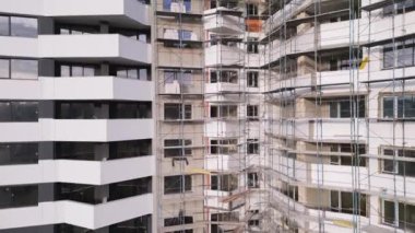İşçiler birden fazla katlı modern bir konut inşaatını tamamlamakla meşguller. Yapıyı çevreleyen yapı, devam eden çalışma ve geliştirmeyi gösteriyor.