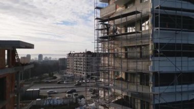 Çalışanlar, canlı bir kentteki yüksek katlı yapıyı yenilerken iskelede görülüyor. Sabahın erken saatlerinde inşaat sahasının üzerine ışık saçıyor ve aşağıdaki aktiviteyi güçlendiriyor..