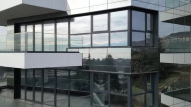 Çağdaş bir binanın çarpıcı tasarımı manzarayı yansıtan geniş cam paneller sergiliyor. Yeşilliklerle çevrelenen yapı, modern estetik ve işlevselliği vurguluyor..