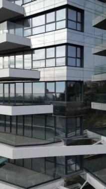 Parlak cam ve beton yapı modern mimari tasarımı sergiliyor. Çevredeki manzaranın yansımaları, parlak gün ışığında binaların yenilikçi tarzını ve zarafetini vurgular..