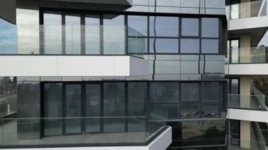 Geniş cam balkonları, temiz hatları ve geometrik şekilleri ile çağdaş mimari sergilenen çok katlı bir bina, kentsel ufuk çizgisini ve yakınlardaki çevreyi yansıtıyor..