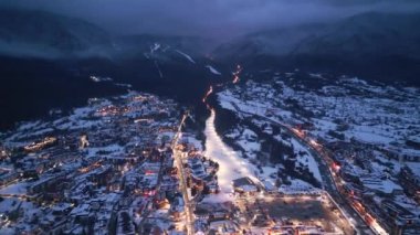 Çarpıcı bir manzara, dağlık bir bölgedeki şehir ışıklarıyla aydınlatılmış bir kış manzarasını yakalıyor. Kar zemini kaplıyor ve alacakaranlık yaklaşırken huzurlu bir atmosfer yaratıyor. Bansko, Bulgaristan