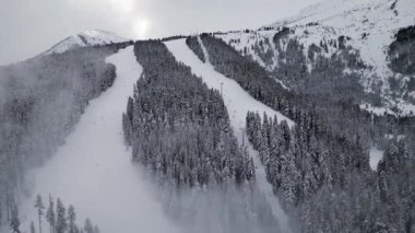 Kar kaplı kayak yamaçları sık ve yeşil ağaçlardan oluşan bir ormana iniyor. Bulutlar bazı zirvelere gölge düşürür ve kış harikalar diyarı atmosferi yaratır. Bansko, Bulgaristan