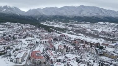 Kış boyunca dağlarda yuva yapmış karla kaplı bir kasabanın havadan görünüşü. Çatılar beyazlarla kaplı ve manzara sakin bir atmosfer sergiliyor. Bansko, Bulgaristan