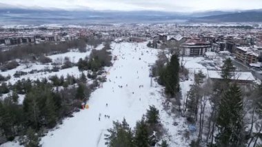 İnsanlar güzel ağaçlar ve uzak tepelerle çevrili güzel bir dağ kasabasını keşfederken kayak yapıyor ve karla kaplı bir arazide yürüyorlar. Bansko, Bulgaristan