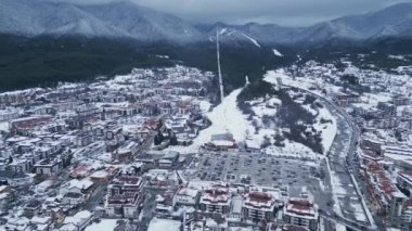 Karla kaplı pitoresk bir dağ kasabasında tuhaf bir cazibesi olan binalar yer alıyor. Arka planda, gri gökyüzüne doğru yükselen bir kayak yamacı kış cazibesini artırıyor. Bansko, Bulgaristan