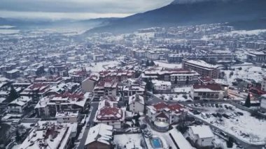 Karla kaplı bir kasabanın havadan görünüşü, bulutlu bir günde arka planda dağlar olan karla kaplı binaların arasında sarmalanmış çatılar ve caddeleri gösteriyor. Bansko, Bulgaristan