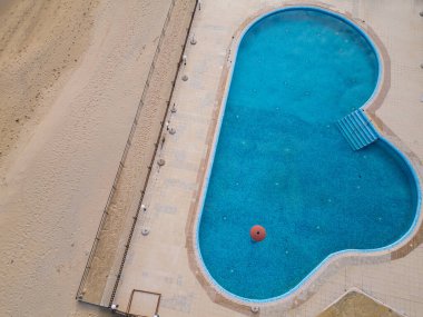 Kalp şeklinde bir yüzme havuzu, açık mavi gökyüzünü yansıtan kumlu bir plajın yanında davetkâr bir şekilde durur. Bölge iyi korunmuş, rahatlama ve rahatlama için ideal..