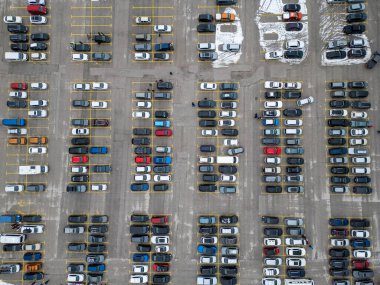 Büyük bir otopark farklı renk ve modellerden oluşan arabalarla doludur. Yukarıdan bakıldığında, yerde biraz kar görünen düzenli park halindeki araçlar görülüyor..