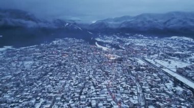 Panoramik bir manzara, alacakaranlıkta yükselen dağlarla çevrili karla kaplanmış pitoresk bir kasaba ortaya çıkarıyor. Işıklar çatılarda parıldıyor, sakin bir atmosfer yaratıyor. Bansko, Bulgaristan