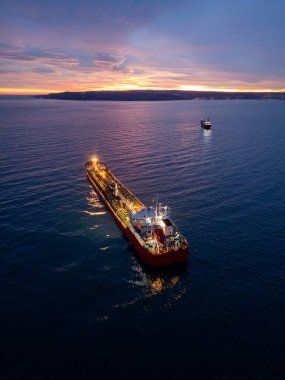 Alacakaranlıkta açık deniz ve ışıldayan ufukla çevrili parlak bir tanker gemisinin havadan görüntüsü..