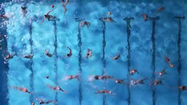 Parlak mavi bir havuzda su topu antrenmanının yukarıdan aşağı görüntüsü. Hareket eden ve su sıçratan oyuncular sporun enerjisini ve koordinasyonunu yakalıyorlar. Takım ve atletik temalar için mükemmel..