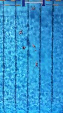 Parlak mavi bir havuzda su topu antrenmanının yukarıdan aşağı görüntüsü. Hareket eden ve su sıçratan oyuncular sporun enerjisini ve koordinasyonunu yakalıyorlar. Takım ve atletik temalar için mükemmel..